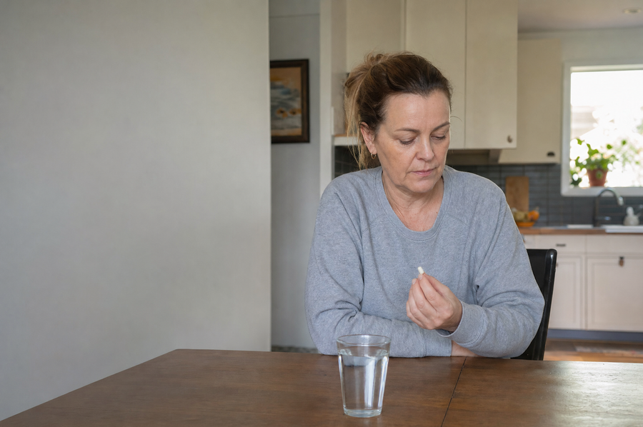 Frau am Küchentisch mit einem Glas Wasser und einer Kapsel