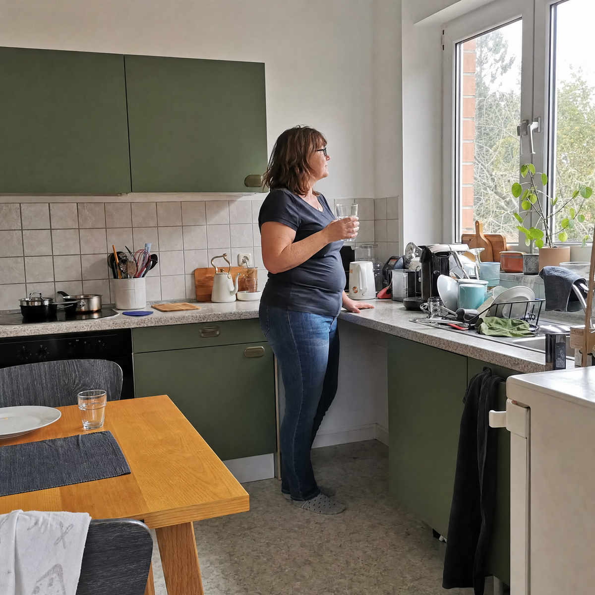 Frau um 50 in ihrer Küche am Morgen, mit einem Glas Wasser
